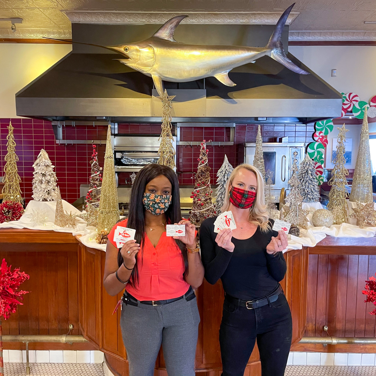 Two San Diego Fish Market Employees standing in front of the bar decorated for the holidays with gift cards in their hands