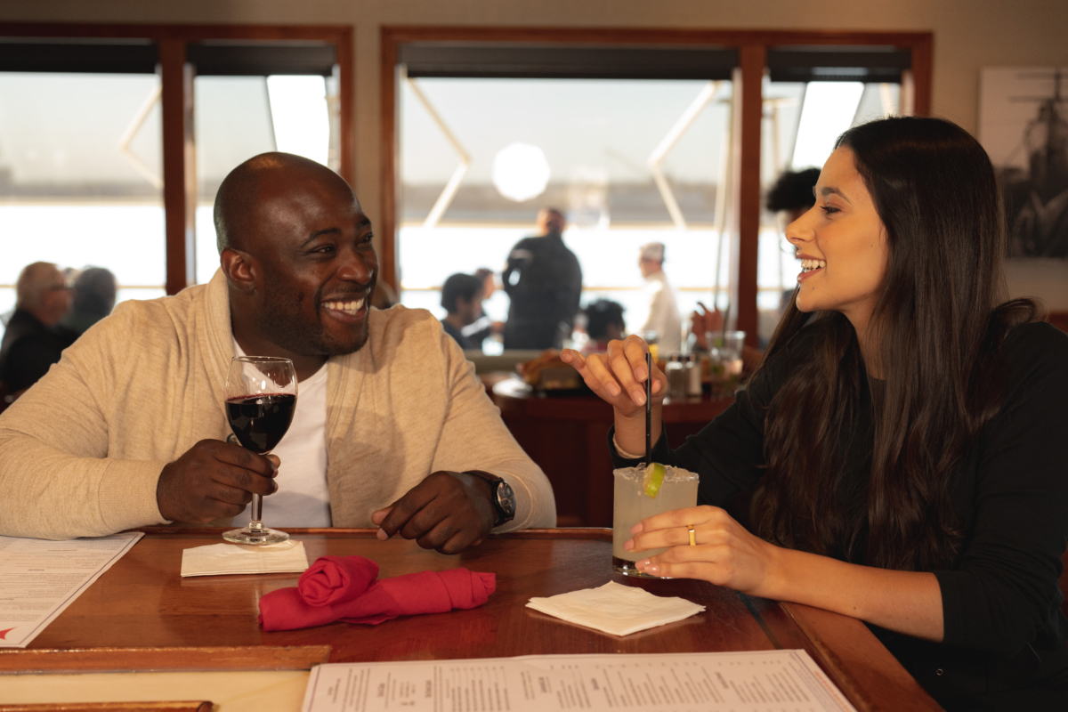 A male guest enjoys a glass of red wine while chatting with a female guest enjoying a cocktail at the bar